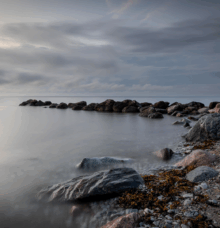 Stenar vid en stillsam kust under en molnig himmel i skymningen.