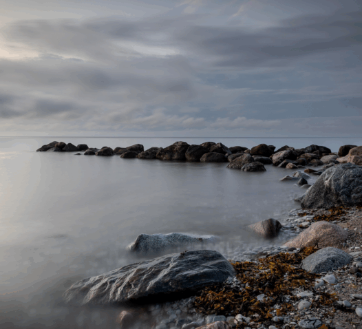 Stenar vid en stillsam kust under en molnig himmel i skymningen.